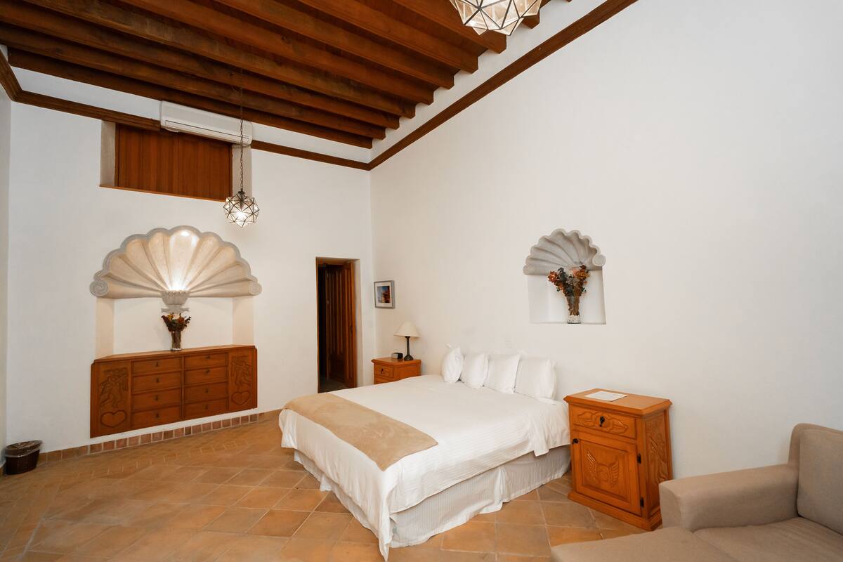 A bedroom with a large bed, wooden headboard, a nightstand, a dresser, and a small cabinet.