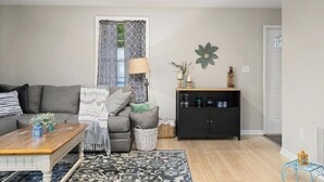 Un salon comprenant un canapé, une table basse, un tapis à motifs, un meuble décoratif et une fenêtre agrémentée de rideaux à motifs.