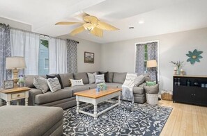 A living room with a grey sofa, a wooden coffee table, patterned rug, and a ceiling fan.