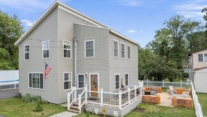 Une maison à deux étages avec une terrasse à l’avant et un espace aménagé pour s’asseoir à l’extérieur.