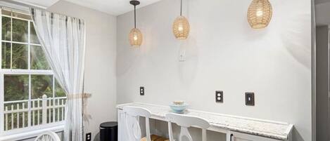 A dining area with a white table and chairs, three hanging pendant lights, and a window with curtains.