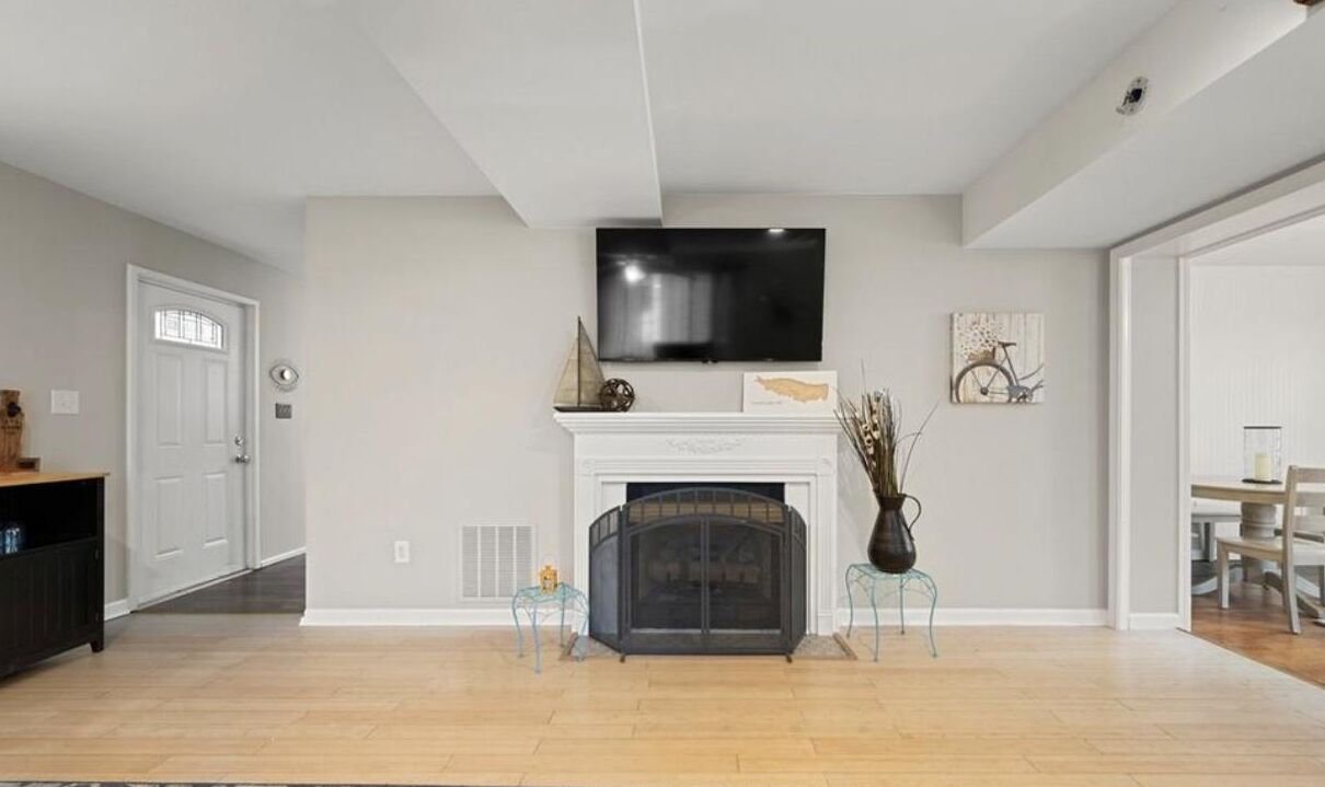 A living room with a fireplace, a television mounted above it, and a dining area visible through an open door.