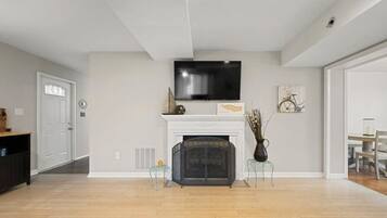 A living room with a fireplace, a television mounted above it, and a dining area visible through an open door.