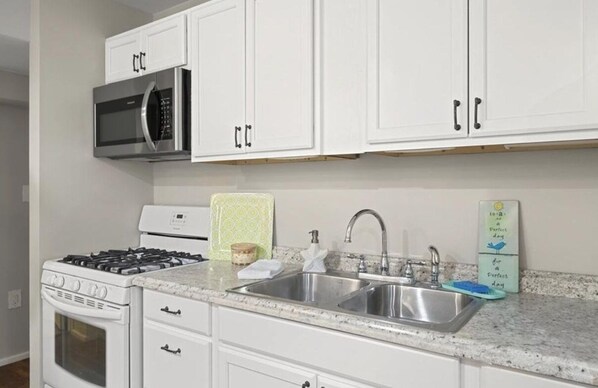 A kitchen with white cabinets, a stainless steel sink, a microwave, a stove, and a toaster.