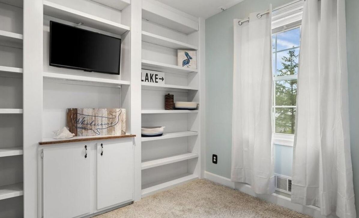 A neatly organized room with built-in shelving, a flat-screen TV, and a window with curtains.