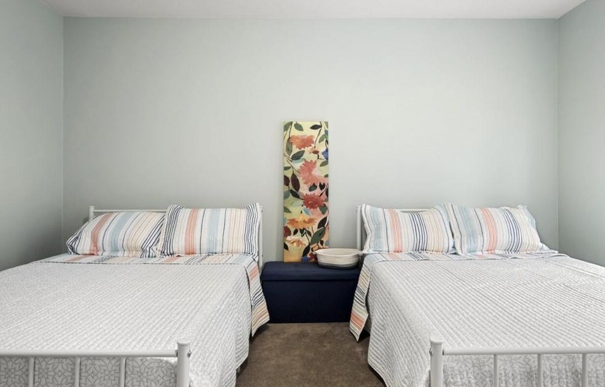 A bedroom with two single beds, a nightstand, a decorative wall piece, and a light-colored carpet.