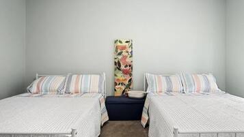 A bedroom with two single beds, a nightstand, a decorative wall piece, and a light-colored carpet.