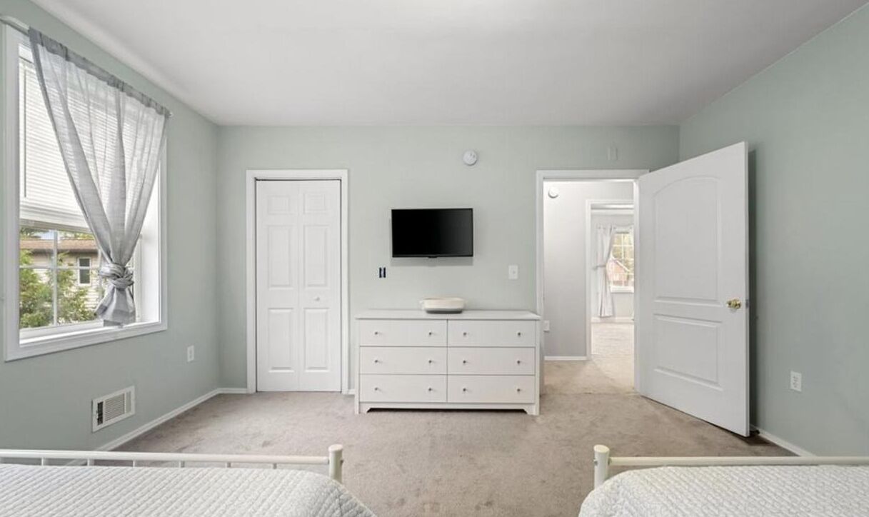 Un dormitorio con cama, cómoda, televisor y ventana con cortinas.