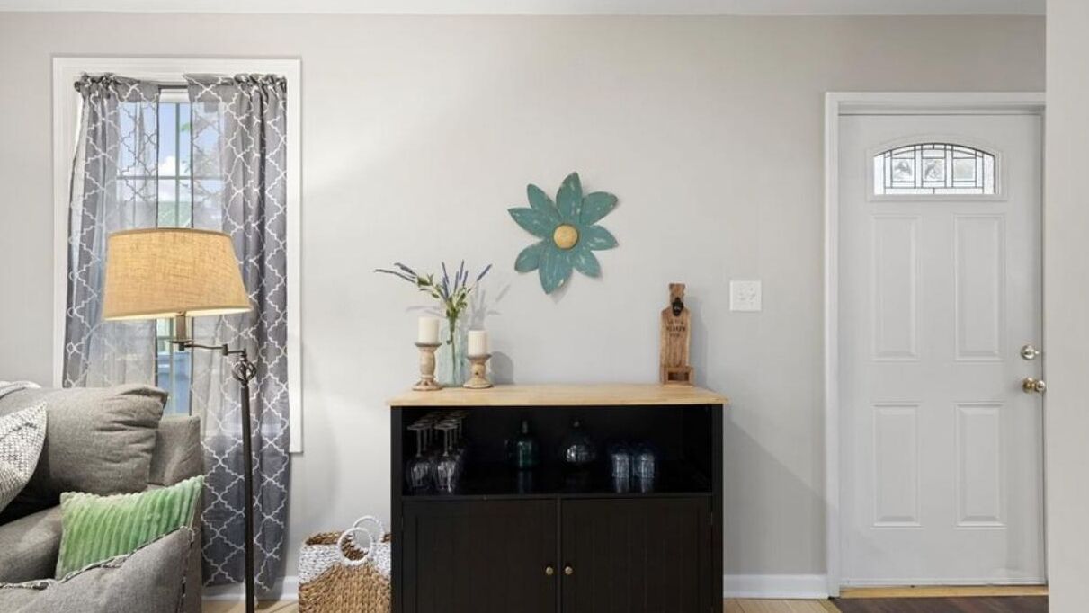 Een woonkamer met een bank, een lamp, een decoratief wandobject en een kast met glazen.