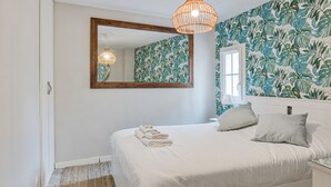 Een slaapkamer met een groot bed, een spiegel, een hanglamp en een raam met gordijnen.