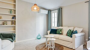 Een woonkamer met een witte bank, een klein rond tafeltje, een geweven vloerkleed en een hanglamp.