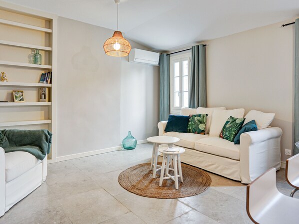 A living room with a white sofa, a small round table, a woven rug, and a hanging light fixture.