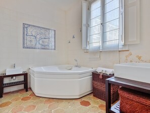 Ein Badezimmer mit einer großen Badewanne, einem kleinen Waschbecken, einer Karte an der Wand und einem Fenster mit Jalousien.