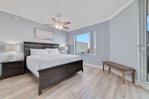 Ein Schlafzimmer mit Bett, Nachttischen, einer Bank, einem Deckenventilator und einem Fenster.