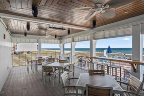 Eine überdachte Terrasse mit Tischen und Stühlen mit Blick auf Strand und Meer.