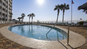 Una piscina con il sole riflesso sull'acqua, circondata da lettini e palme, con un edificio sullo sfondo.
