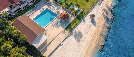 An aerial view of a beachfront hotel with a swimming pool, beach access, and lush greenery.