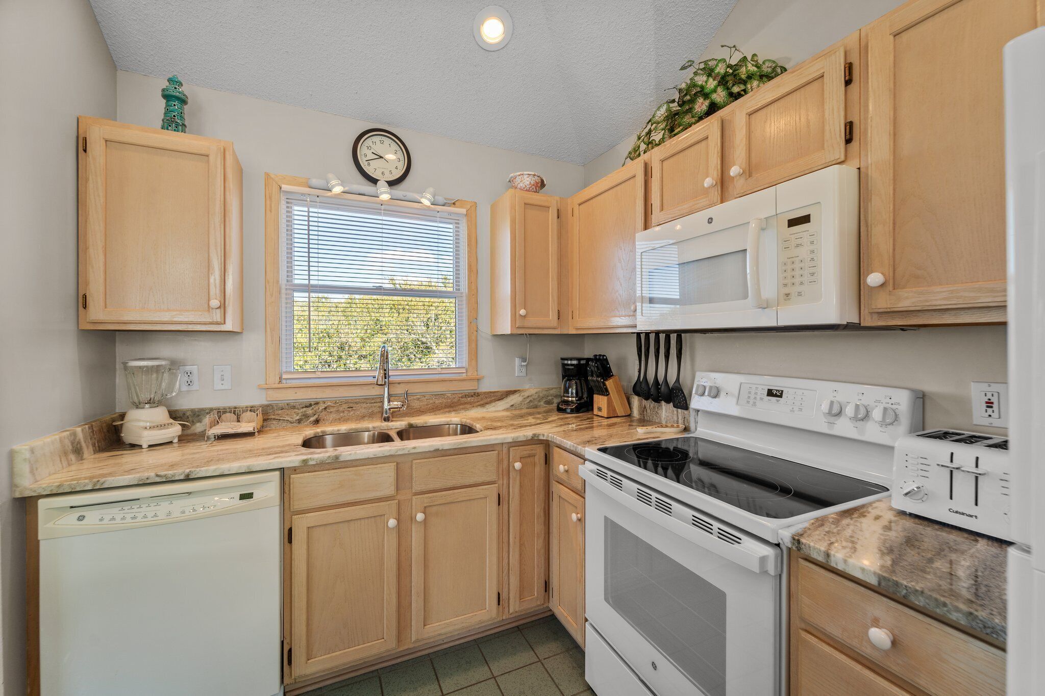 A kitchen with wooden cabinets, a microwave, a stove, a dishwasher, and a window with blinds.