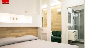 Une chambre d’hôtel moderne équipée d’un lit, d’un canapé vert, d’un dressing et d’un espace douche.