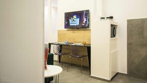 Une petite cuisine équipée d’un micro-ondes, d’un téléviseur diffusant un dessin animé et d’un comptoir avec des chaises.