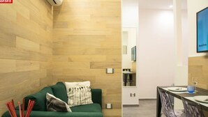 Une chambre d’hôtel moderne avec un mur en bois, un canapé vert, une table à manger avec des chaises et un petit coin cuisine.