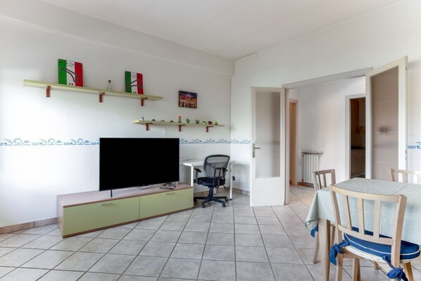 A living room with a TV, a desk, a chair, and a dining table.