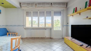 Ein Zimmer mit einem Bett, einem Fernseher, einer Heizung, einem Fenster mit Jalousien und einem Regal mit Gegenständen.