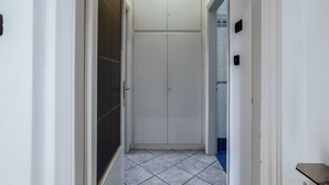 Ein schmaler Flur mit Fliesenboden, einer weißen Tür und einem weißen Schrank mit Tür.