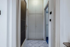 A narrow hallway with a tiled floor, a white door, and a white closet with a door.