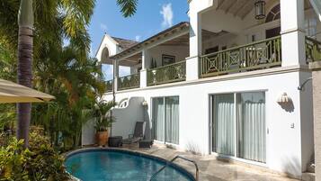 A two-story building with a swimming pool, outdoor seating, and a balcony with green railings.