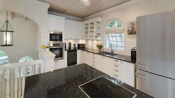 A modern kitchen with white cabinetry, a black granite countertop, stainless steel appliances, and a large island with a built-in stovetop.