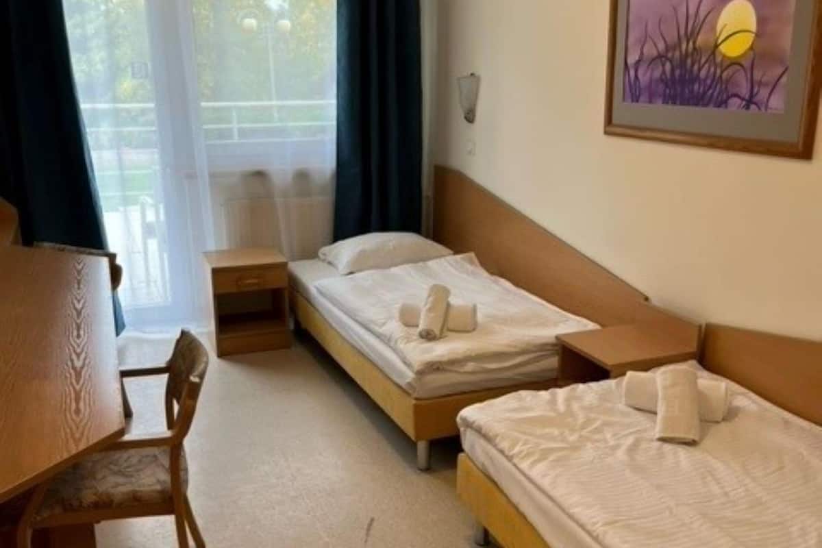 Quarto de hotel com duas camas de solteiro, uma escrivaninha de madeira e uma cadeira.