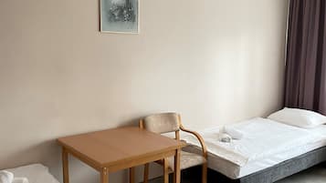 A hotel room with a bed, a small table, a chair, and a single wall-mounted painting.