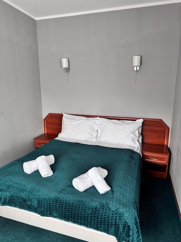 A hotel room with a single bed, a wooden nightstand, a green textured bedspread, and two white towels. - Geovita Jadwisin (Serock)