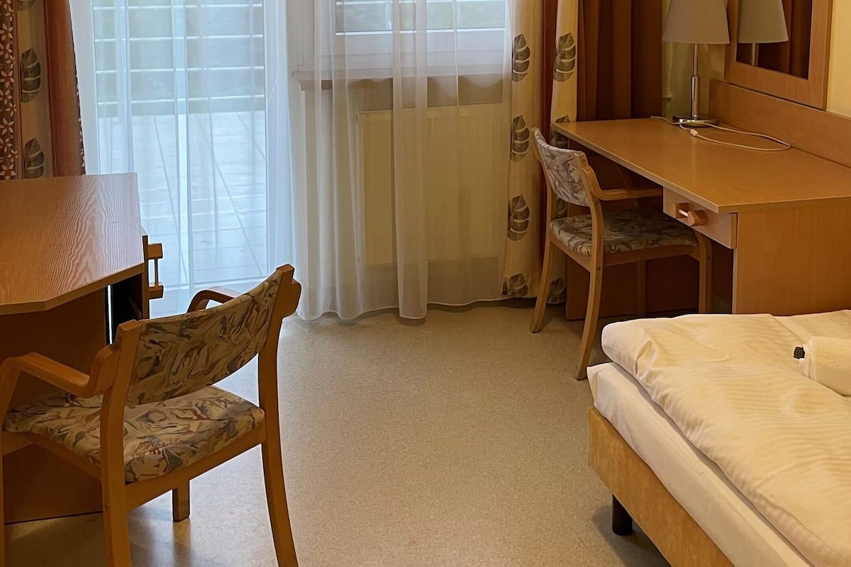Habitación de hotel con cama, escritorio con silla, televisor y ventana con cortinas.