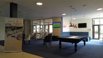 A hotel lobby with a pool table, seating area, and a television screen displaying a sports event.