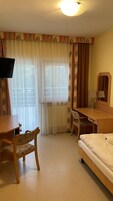 A hotel room with a bed, a desk with a chair, a television, and a window with curtains.