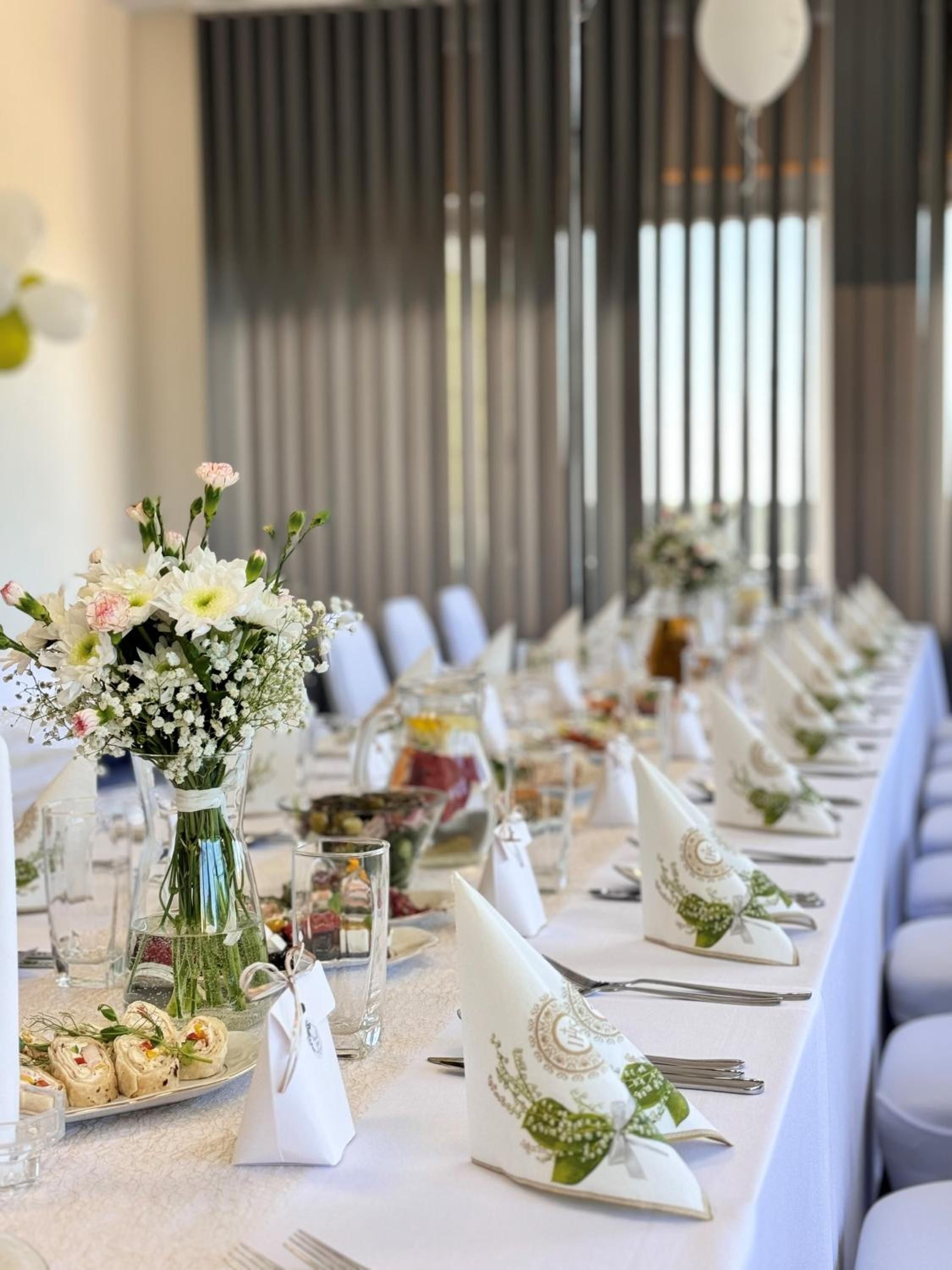 A long dining table set with white tablecloths, glassware, and floral centerpieces.