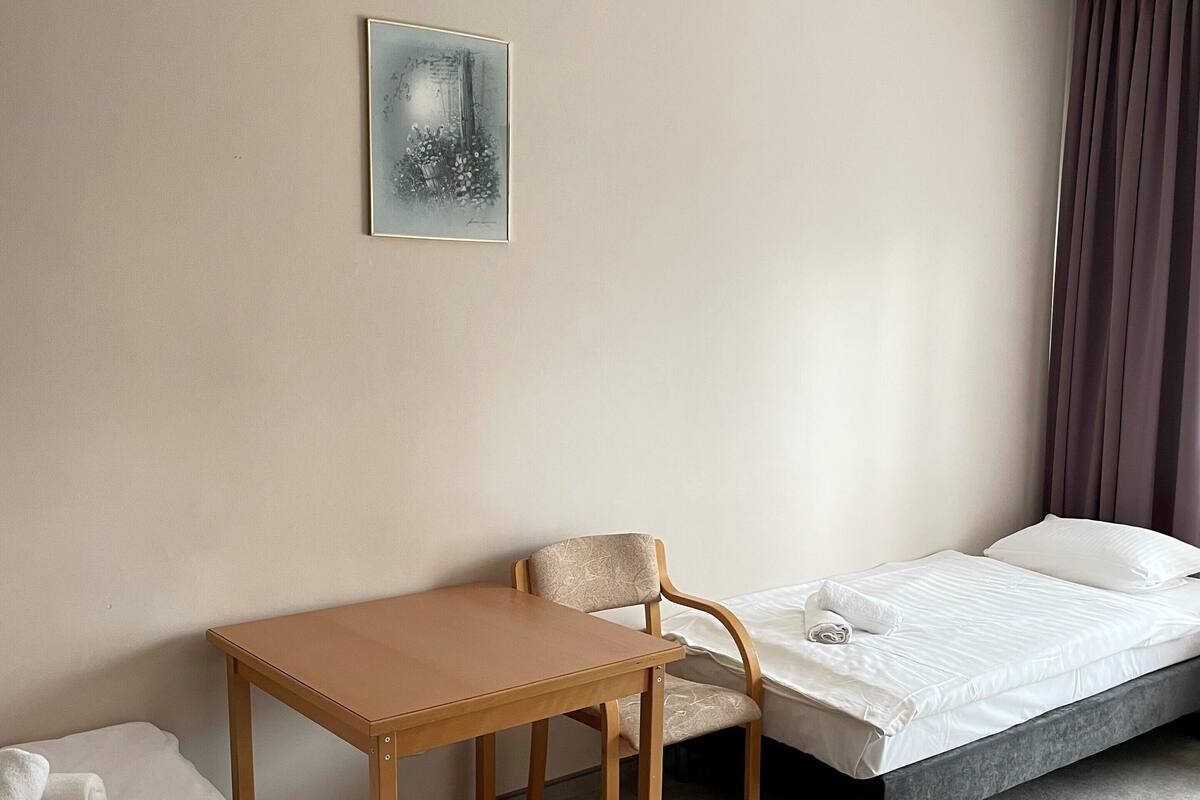 Quarto de hotel com uma cama, uma mesa pequena, uma cadeira e um quadro pendurado na parede.