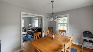 Ein Essbereich mit Holztisch und -stühlen, einer Kristallleuchter und Blick auf ein Wohnzimmer mit Sofa und Fenster.