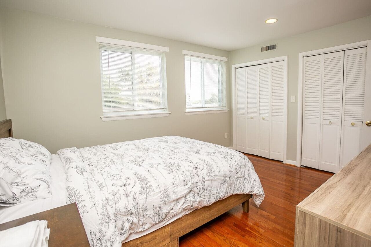 A bedroom with a bed, two windows, and a set of closets.