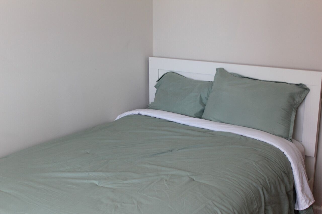 Ein Bett mit weißem Kopfteil und grüner Bettwäsche in einem Raum mit schlichten Wänden.