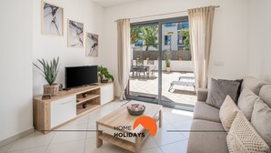 Ein modernes Wohnzimmer mit Sofa, Fernseher und Couchtisch, ein Balkon mit Gartenmöbeln sowie gerahmte Kunstwerke an den Wänden.