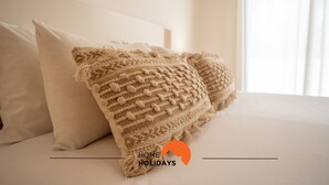 Ein Bett mit zwei beigen Kissen und einer gemusterten Decke.