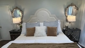 A neatly made bed with a white duvet and a brown throw blanket, flanked by two nightstands with lamps and a mirror.