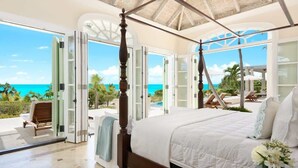 Une chambre à coucher avec un lit à baldaquin, de grandes portes vitrées donnant sur une piscine et une vue sur l’océan.