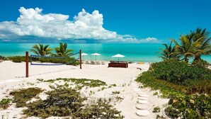 Une plage avec un filet de volley-ball, des chaises longues et des parasols.