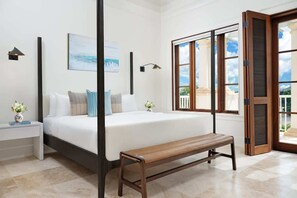 A bedroom with a large bed, a bench, a nightstand, a wall-mounted lamp, and a window with a view. - Villa Shambhala 3 BR (Long Bay)