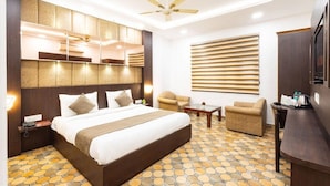 A hotel room with a large bed, a ceiling fan, a sofa, a small table, and a TV. - Hotel Panickers Residency (New Delhi)