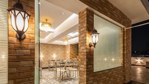 A dining area with a brick wall, glass partition, and a chandelier. - Hotel Panickers Residency (New Delhi)